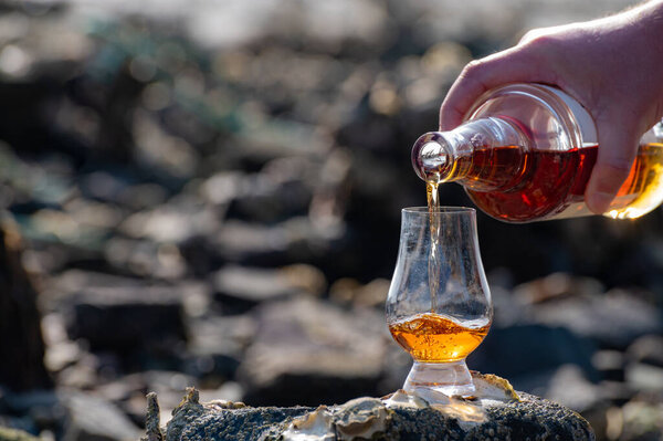 Pouring of Scotch whisky in tasting glass in sunny day