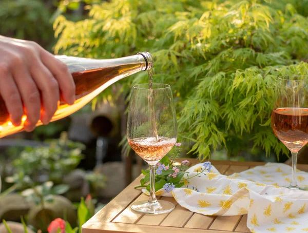 Waiter pouring cold rose wine in glasses on outdoor terrace in garden in sunny day