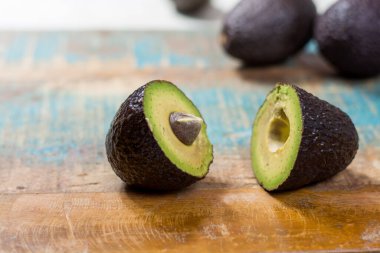 Ahşap arka planda yaprakları olan ham koyu yeşil bir avokado.