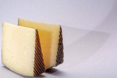İki parça Manchego, queso manchego, İspanya 'nın La Mancha bölgesinde manchega soyundan gelen koyun sütünden yapılan peynir, beyaz üzerine izole edilmiş.