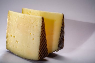 İki parça Manchego, queso manchego, İspanya 'nın La Mancha bölgesinde manchega soyundan gelen koyun sütünden yapılan peynir, beyaz üzerine izole edilmiş.