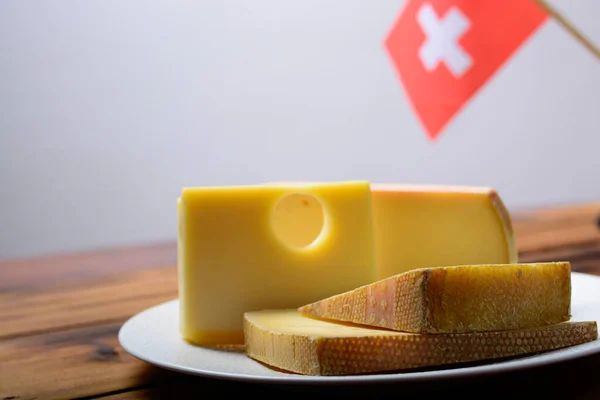 Assortment of Swiss cheeses Emmental or Emmentaler medium-hard cheese with round holes, Gruyere, appenzeller and raclette used for traditional cheese fondue and gratin and flag of Switzerland