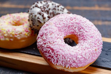 Siyah ahşap arka planda fırından alınmış renkli tatlı donutlar.