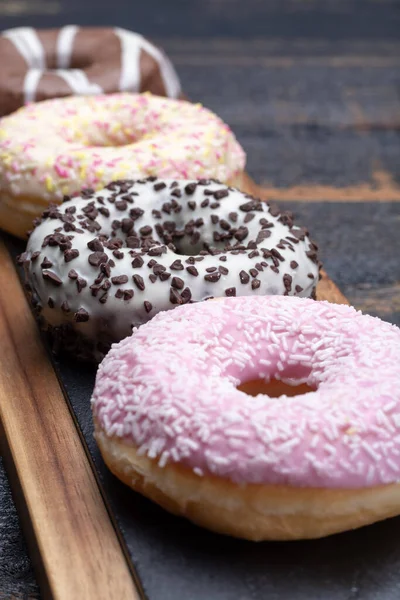 Colorful sweet glazed donuts from bakery on black wooden background close up