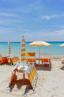 Plaj ekipmanları, sandalyeler ve güneş şemsiyesi açık mavi deniz suyu, plaj tatili konsepti