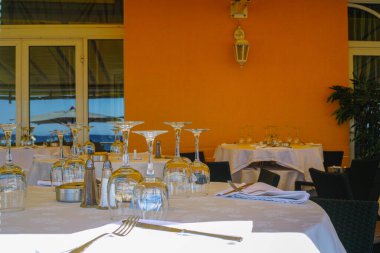 Fransız Rivierası 'ndaki şık restoran misafirleri bekliyor. Bardaklar, sofra takımı ve beyaz keten peçetelerle yemek masası servis ediyor.