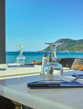 Fransız Rivierası 'nda deniz manzaralı şık bir kafe misafirleri bekliyor. Bardaklar, masa örtüleri ve peçetelerle yemek masası servis ediyor.