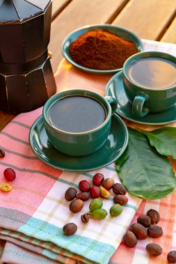 Sade kahve ile servis edilen, çiğ yeşil, olgun kırmızı ve kavrulmuş kahve çekirdekleri, yakın kahve fabrikasından yeşil yapraklarla süslenmiş.