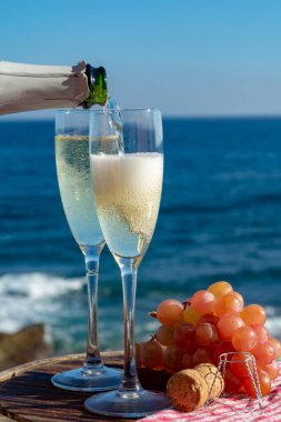 Garson şampanyayı, kovboyu ya da kavayı terasta iki bardakta dolduruyor. Deniz manzaralı.
