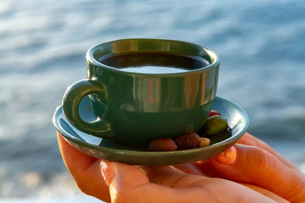 Cup with black coffee in hands with sea view on background