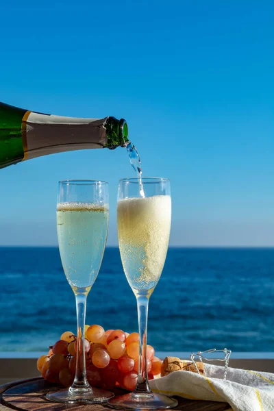 Waiter pouring Champagne, prosecco or cava in two glasses on outside terrace with sea view  close up