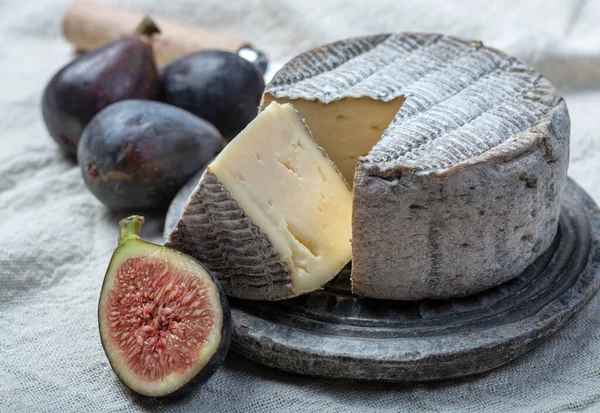 丸みを帯びた成熟したフランスのトムチーズには 黒ブドウと新鮮な熟したイチジクが閉じられた1つのカットピースが付いています — ストック写真