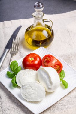 Beyaz İtalyan peyniri Mozzarella bufalosu taze domates, zeytin yağı ve beyaz arka planda yeşil fesleğen yapraklarıyla servis edilir.