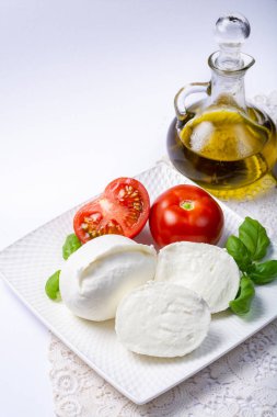Beyaz İtalyan peyniri Mozzarella bufalosu taze domates, zeytin yağı ve beyaz arka planda yeşil fesleğen yapraklarıyla servis edilir.
