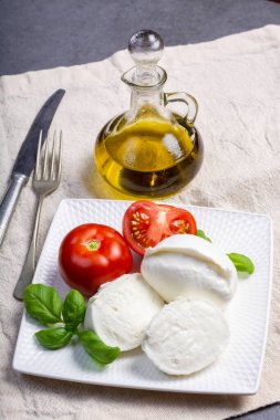 Beyaz İtalyan peyniri Mozzarella bufalosu taze domates, zeytin yağı ve beyaz arka planda yeşil fesleğen yapraklarıyla servis edilir.