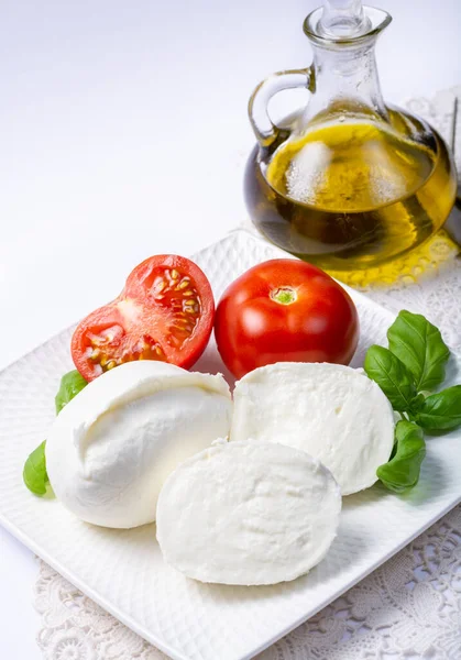 柔らかい白いイタリアチーズ新鮮なトマト オリーブオイル 白い背景の緑のバジルの葉で提供されるモッツァレラチーズの水牛 — ストック写真