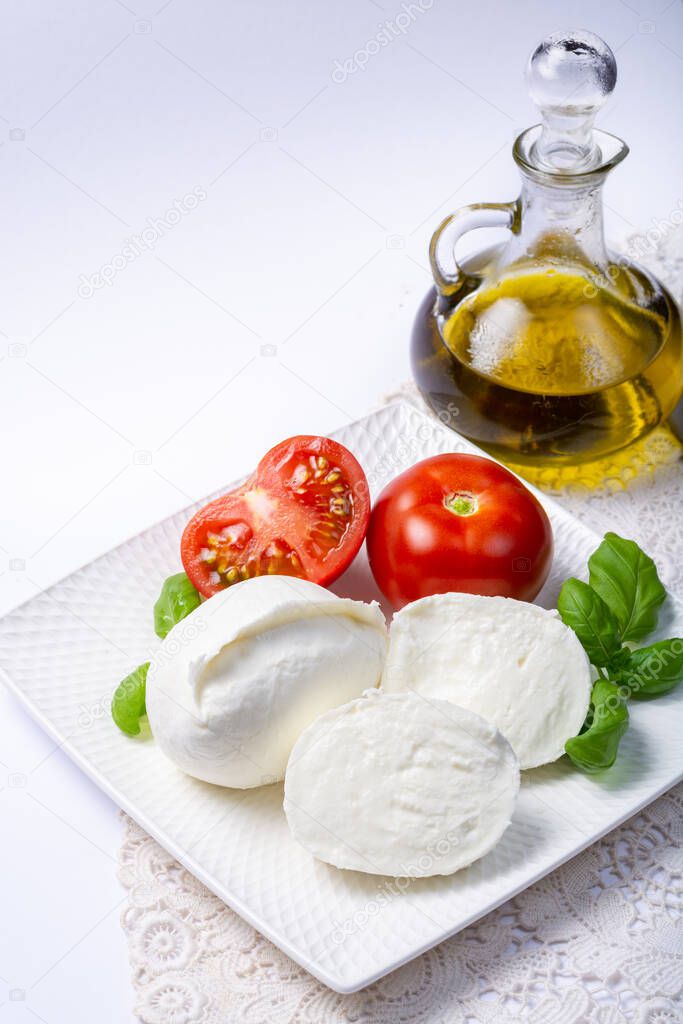 Soft white Italian cheese Mozzarella buffalo served with fresh tomato, olive oil and green basil leaves on white background