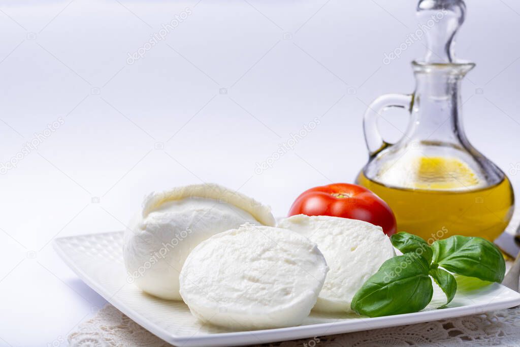 Soft white Italian cheese Mozzarella buffalo served with fresh tomato, olive oil and green basil leaves on white background