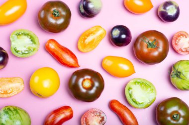 Düz manzaralı yiyecek arka planında çok renkli Fransız taze domatesleri modayı takip eden pembe masa üzerinde yatıyordu.