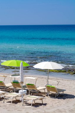 Plaj ekipmanları, sandalyeler ve güneş şemsiyesi açık mavi deniz suyu, plaj tatili konsepti