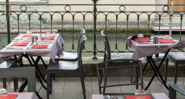 Küçük bir nehirde, ziyaretçiler için servis edilen masalarla dolu boş bir Fransız kafesi veya brasserisi. Yaz tatili.