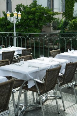 Küçük bir nehirde, ziyaretçiler için servis edilen masalarla dolu boş bir Fransız kafesi veya brasserisi. Yaz tatili.