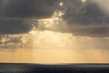 Deniz suyunun üzerinde dramatik bir gün batımı. Gri bulutlar ve güneş ışığı, doğa deniz manzarası.