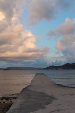 Deniz suyunun üzerinde dramatik bir gün batımı. Gri bulutlar ve güneş ışığı, doğa deniz manzarası.