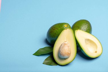 Taze organik olgun yeşil bir bütün ve yapraklarla dilimlenmiş Fuerte avokadosu, kopyalama alanı izole edilmiş modaya uygun mavi arka plan.