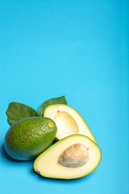 Taze organik olgun yeşil bir bütün ve yapraklarla dilimlenmiş Fuerte avokadosu, kopyalama alanı izole edilmiş modaya uygun mavi arka plan.