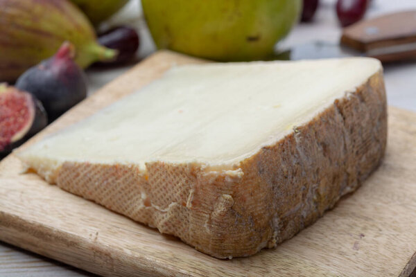 Piece of French cheese Tomme de Brebis made from sheep milk served as dessert with fresh figs and pears close up