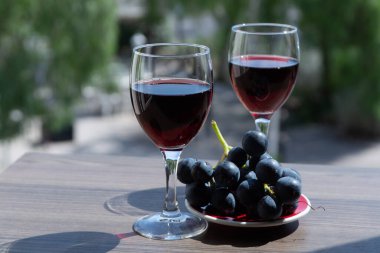 Güneşli yaz gününde, açık terasta kırmızı üzümle servis edilen kırmızı şaraplı iki şarap kadehi.