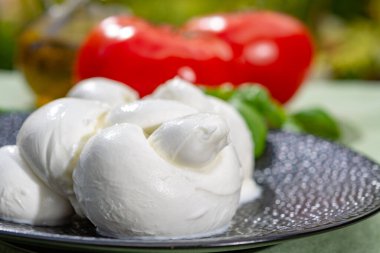 Taze fesleğen ve domatesle servis edilen yumuşak İtalyan mozzarellası şeklinde kıvrılmış.