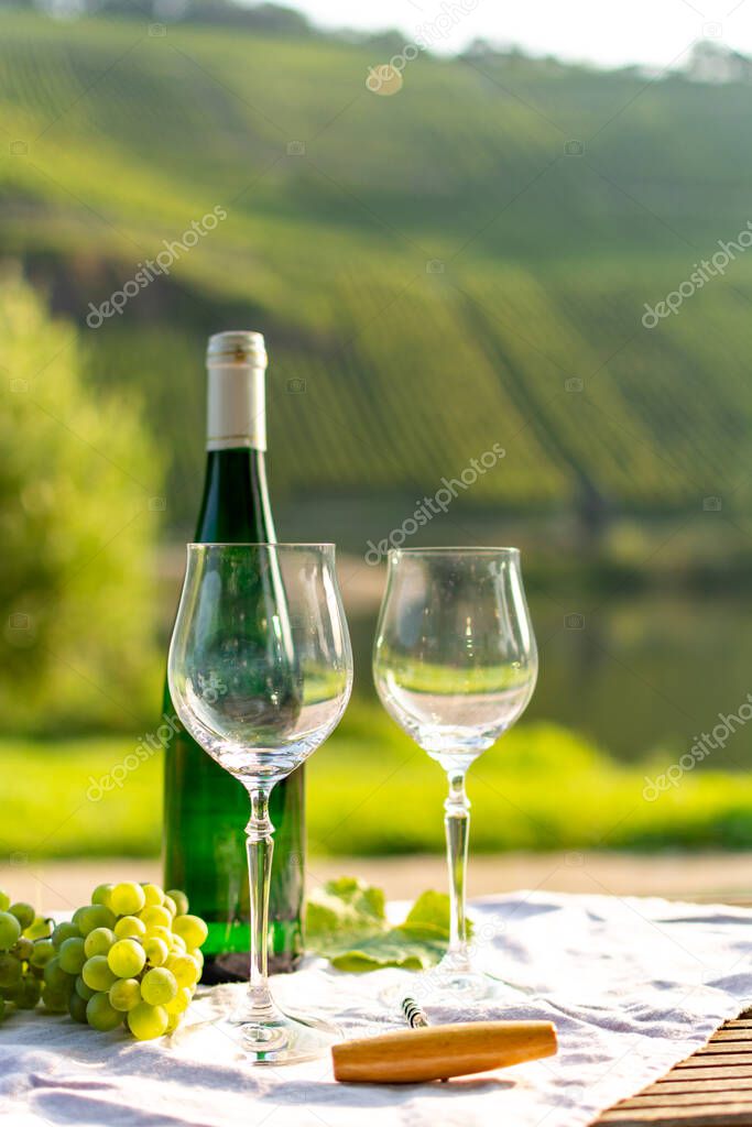 Famous German quality white wine riesling, produced in Mosel wine regio from white grapes growing on slopes of hills in Mosel river valley in Germany, bottle and glasses served outside in Mosel valley