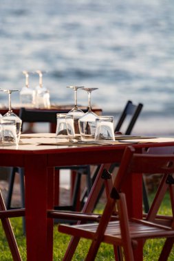 Açık İtalyan kafe veya restoranındaki masalar gün batımında deniz manzaralı sahilde akşam yemeği için servis edilir.