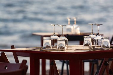 Açık İtalyan kafe veya restoranındaki masalar gün batımında deniz manzaralı sahilde akşam yemeği için servis edilir.