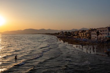 Sperlonga, Lazio, İtalya, yaz tatilinde gün batımında kumlu sahilde insan siluetleriyle manzara