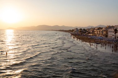 Sperlonga, Lazio, İtalya, yaz tatilinde gün batımında kumlu sahilde insan siluetleriyle manzara