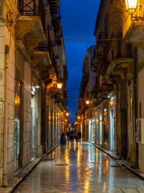 Gece Marsala 'da eski bir cadde yağmur altında sokak lambalarının yansımasıyla, Sicilya, İtalya