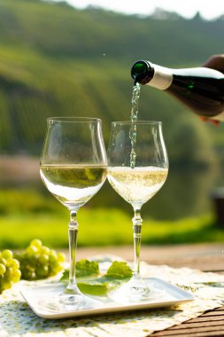 Almanya 'nın Mosel Nehri vadisinde tepelerde büyüyen beyaz üzümlerden elde edilen beyaz üzümlerden üretilen Alman kaliteli beyaz şarap riesling şarabı, Mosel Vadisi' nin dışında servis edilen şişe ve bardaklar.