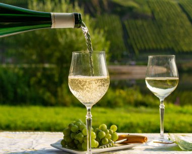 Almanya 'nın Mosel Nehri vadisinde tepelerde büyüyen beyaz üzümlerden elde edilen beyaz üzümlerden üretilen Alman kaliteli beyaz şarap riesling şarabı, Mosel Vadisi' nin dışında servis edilen şişe ve bardaklar.