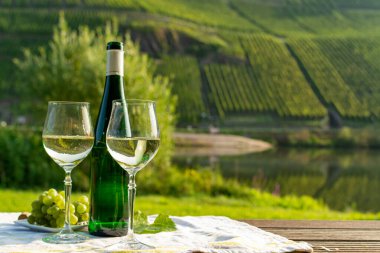 Famous German quality white wine riesling, produced in Mosel wine regio from white grapes growing on slopes of hills in Mosel river valley in Germany, bottle and glasses served outside in Mosel valley clipart