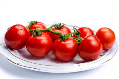 Taze olgun kırmızı domatesler. Tabakta yapraklar ve beyaz arka plan yakın.