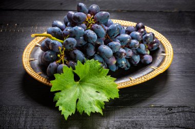 Siyah ahşap arka planda, siyah tabakta servis edilen bir avuç olgun mavi-siyah üzüm.