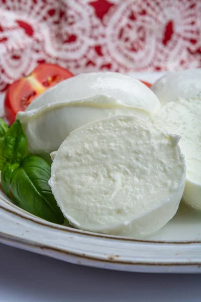 Italian soft cheese mozzarella, white cheese made from cow or buffalo milk with fresh green basil herb and red tomato close up