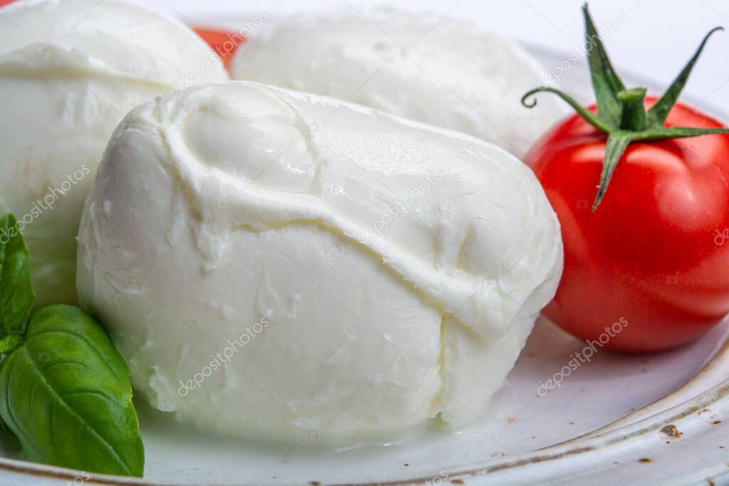 Italian soft cheese mozzarella, white cheese made from cow or buffalo milk with fresh green basil herb and red tomato close up