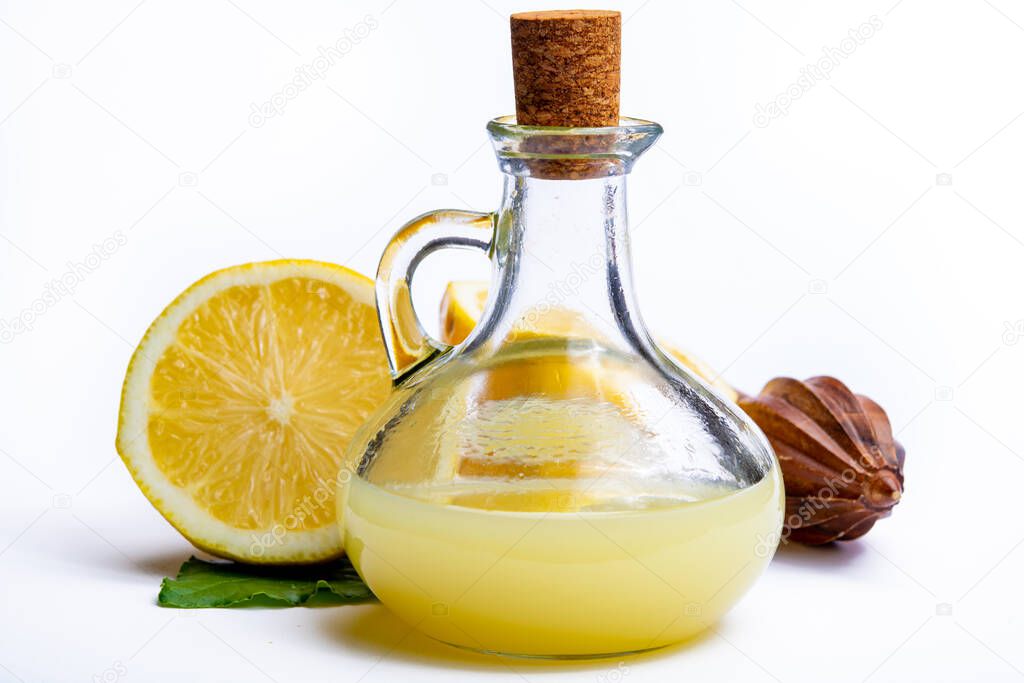 Fresh lemon juice made from ripe yellow Sicilian lemons used for cooking in glass bottle on olive wood plate isolated on white background
