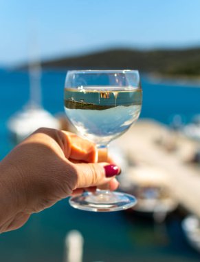 Balkonda servis edilen beyaz şaraplı el ve deniz manzaralı yakın çekim.