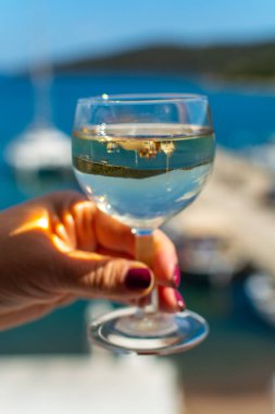 Balkonda servis edilen beyaz şaraplı el ve deniz manzaralı yakın çekim.