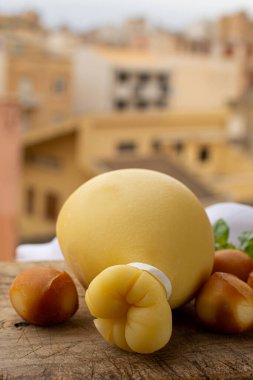 Peynir koleksiyonu, İtalyan provolone caciocavallo yaşlandırılmış ve tütsülenmiş peynirler gözyaşı damlası şeklinde ve arka planda eski İtalyan kasabasının sarı evleri.